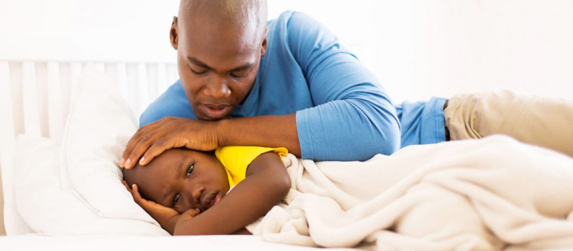 loving african father taking care of his ill son on bed